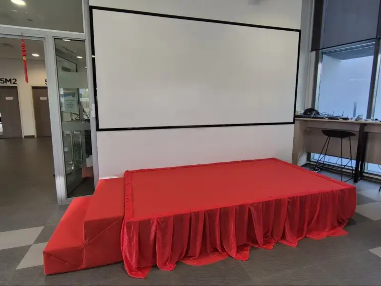 Red carpeted platform stage with red skirting and steps in front of a projector screen in Singapore
